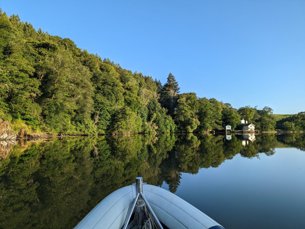 A picture of a tranquil river scene, with woodland and a boathouse